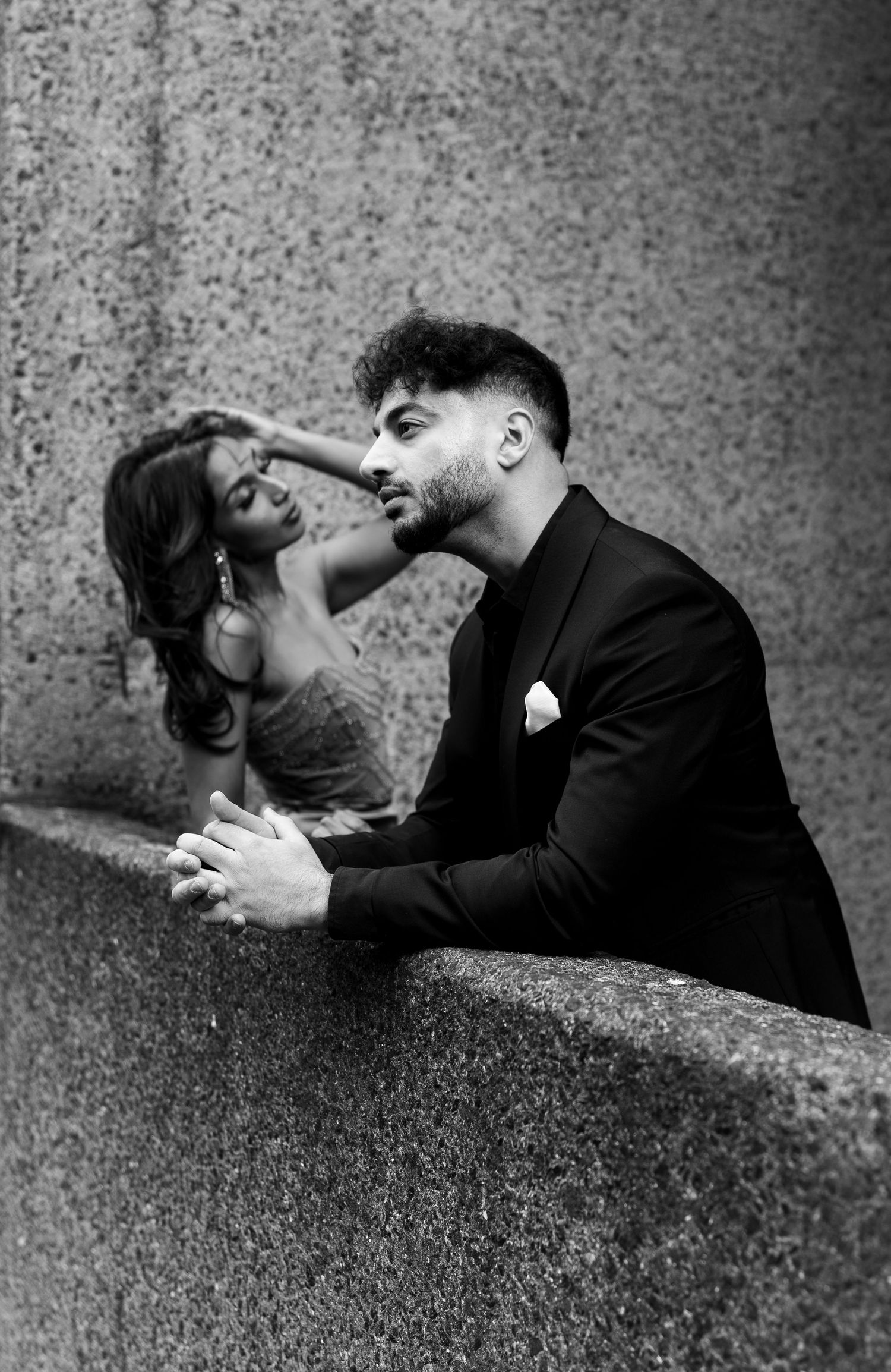 A romantic black and white portrait of a couple in an intimate moment against a textured stone wall.