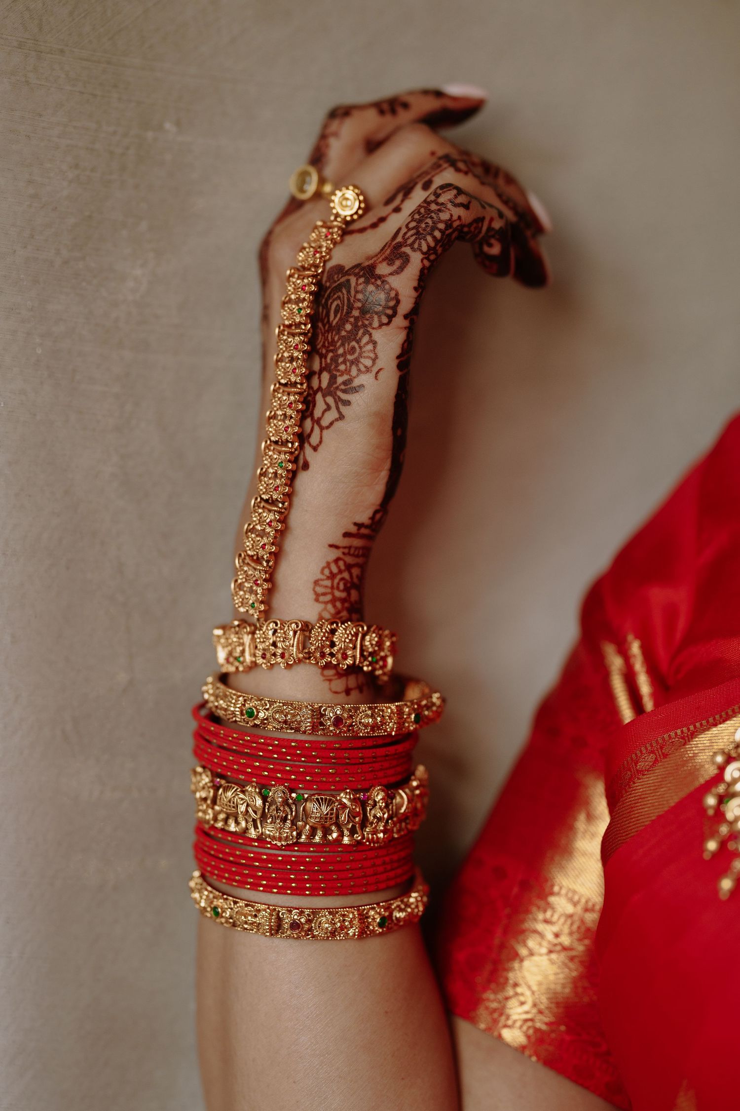 Traditional red chooda bangles with intricate mehndi design and gold bracelets adorning an Indian bride's hand.