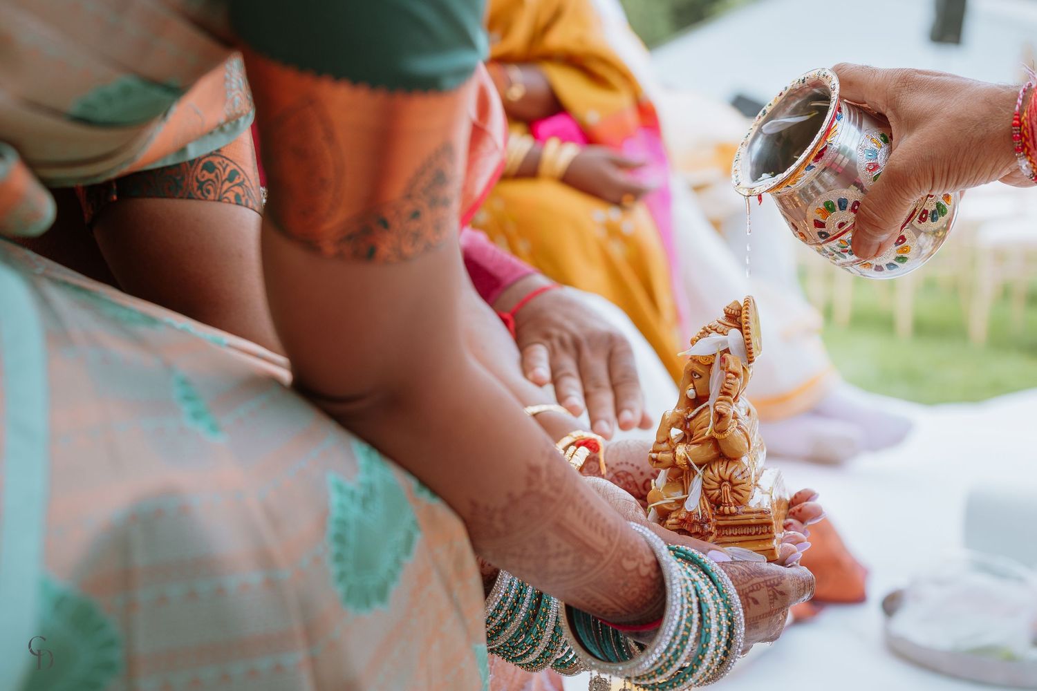 Hands adorned with mehndi and bangles performing traditional Indian wedding rituals.