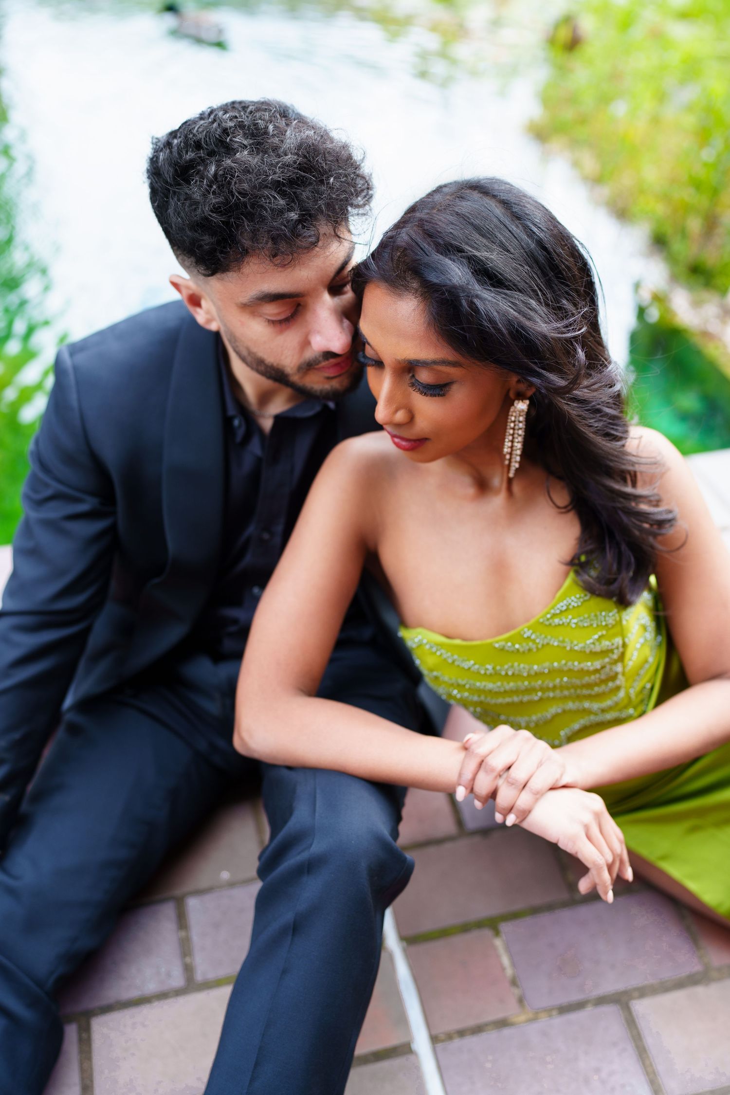 A couple in formal attire sharing a tender moment outdoors with the woman wearing a green dress.