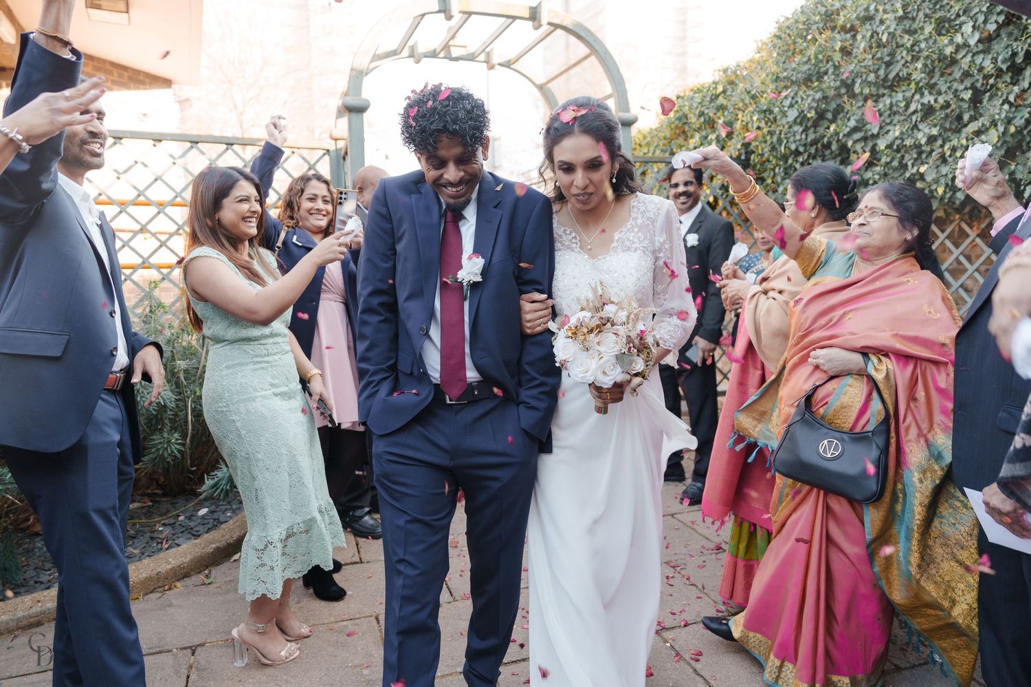 Newlyweds walking through crowd of celebrating guests in outdoor garden setting.