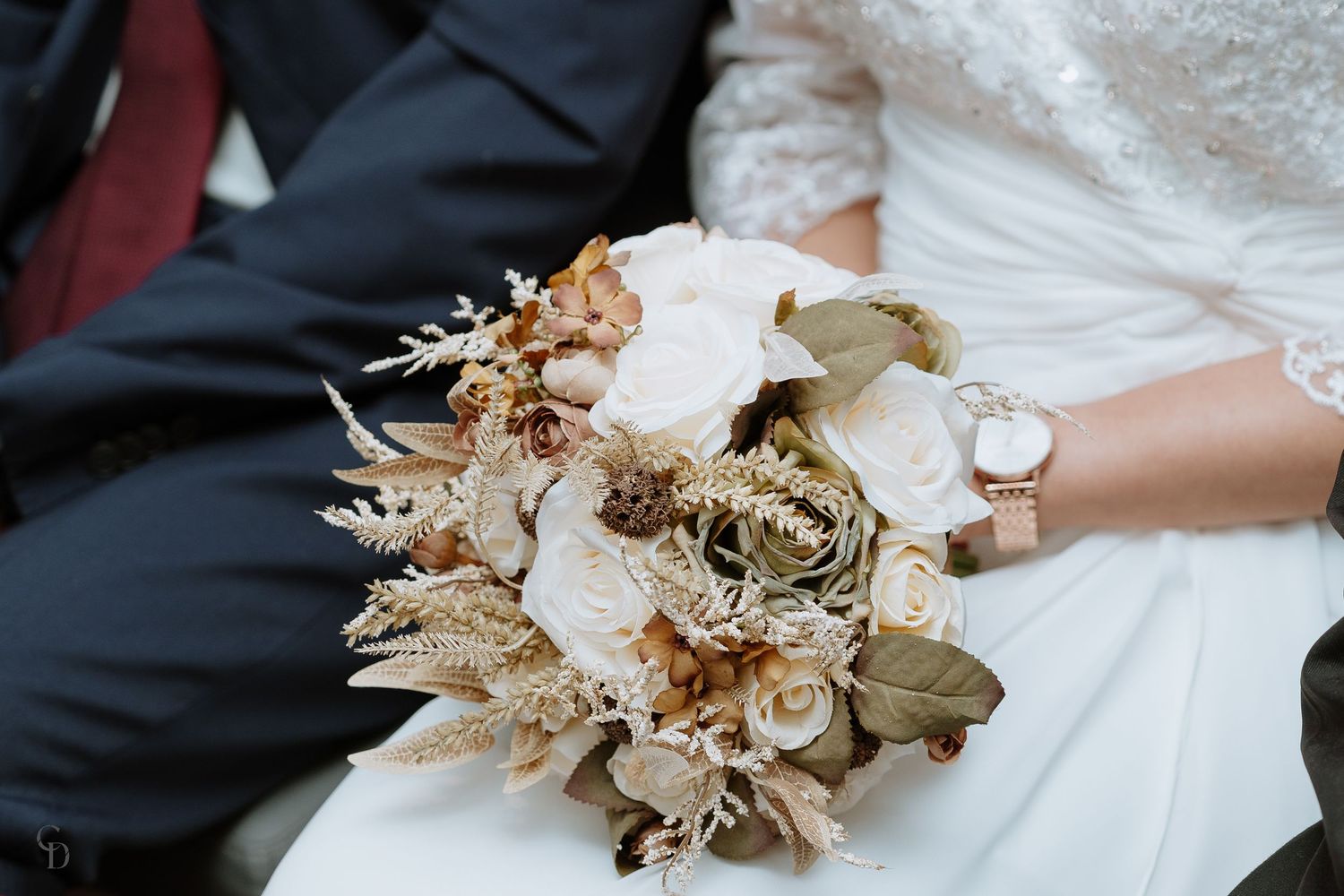 Elegant dried floral wedding bouquet with white and gold tones held against white dress.