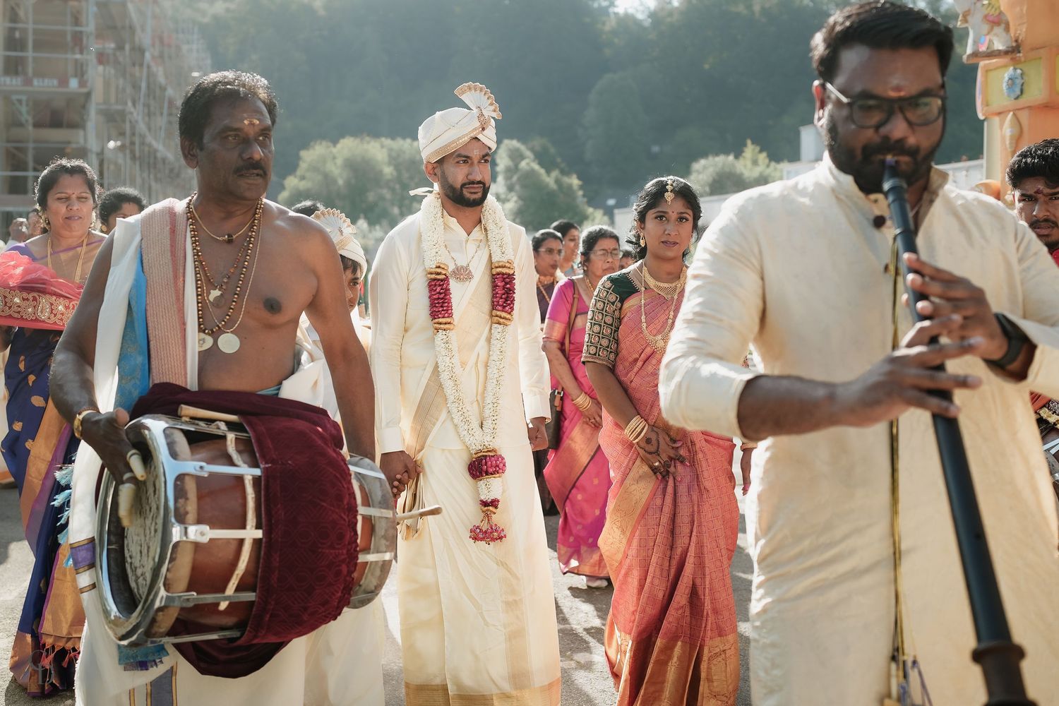 Traditional Indian wedding celebration with drummers, performers and guests in traditional attire during daytime procession.