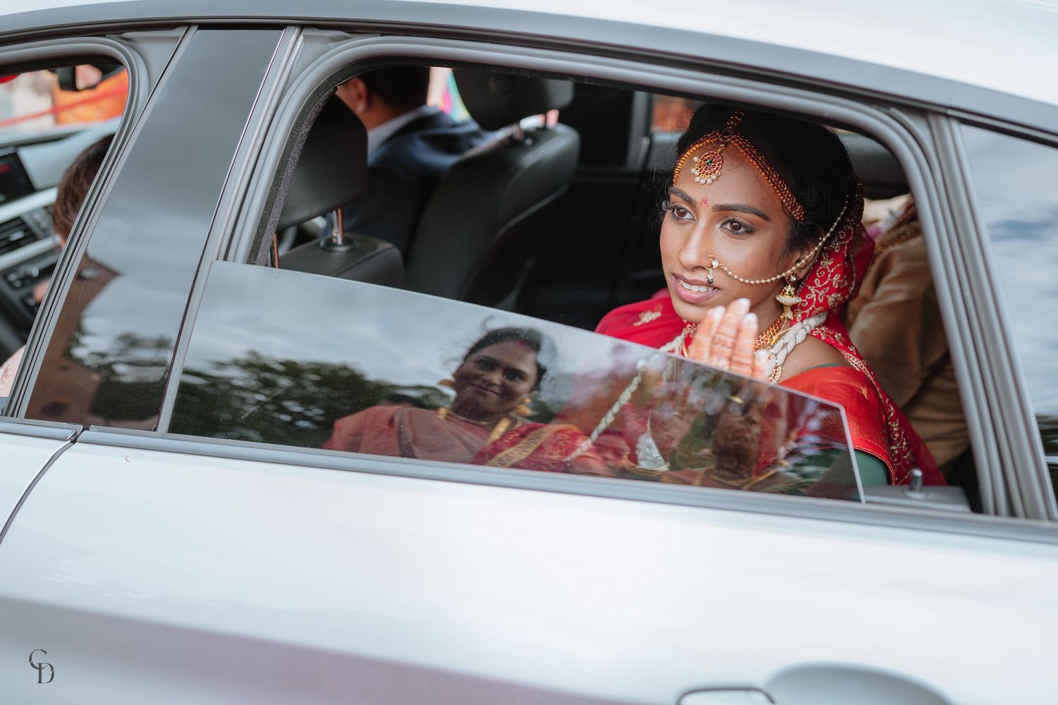 View through car window of someone in traditional red Indian bridal attire.