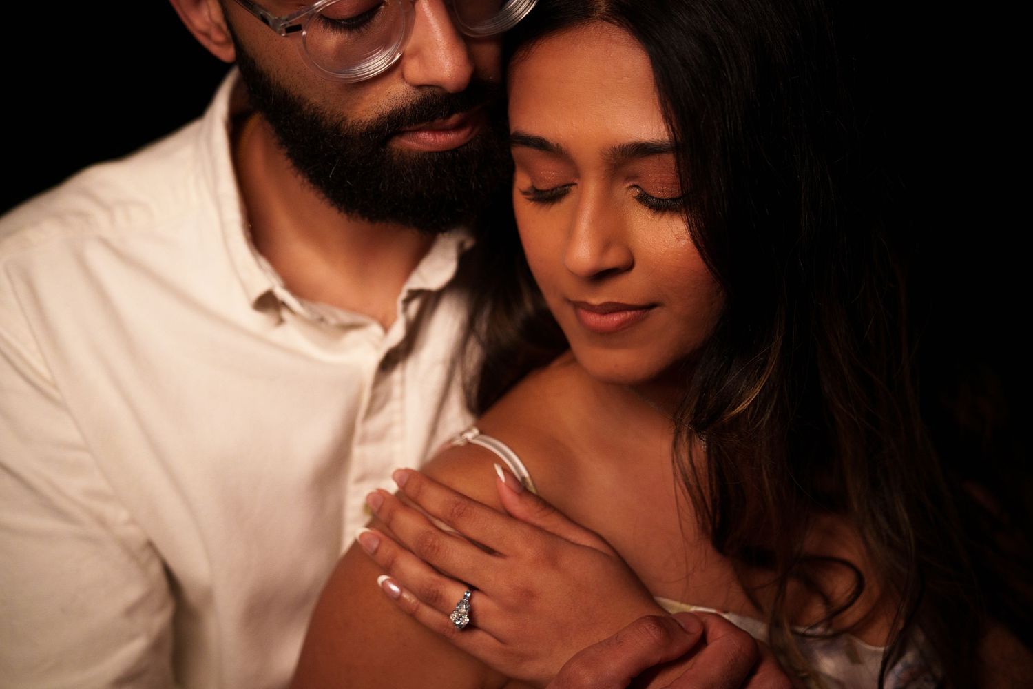 Intimate close-up portrait of couple showing engagement ring in warm lighting.
