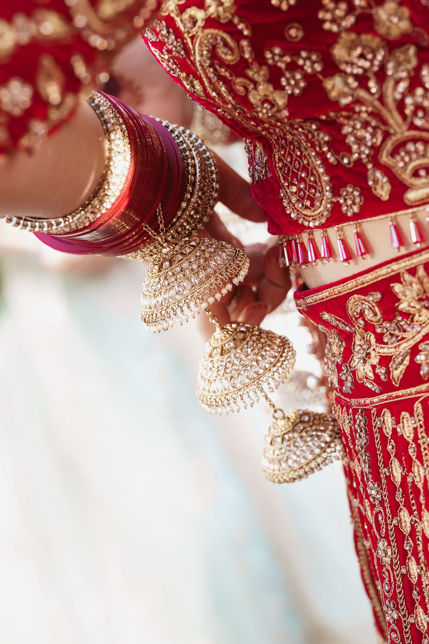 Close-up of Indian bride in red and gold lehenga with ornate jhumka earrings and bangles.