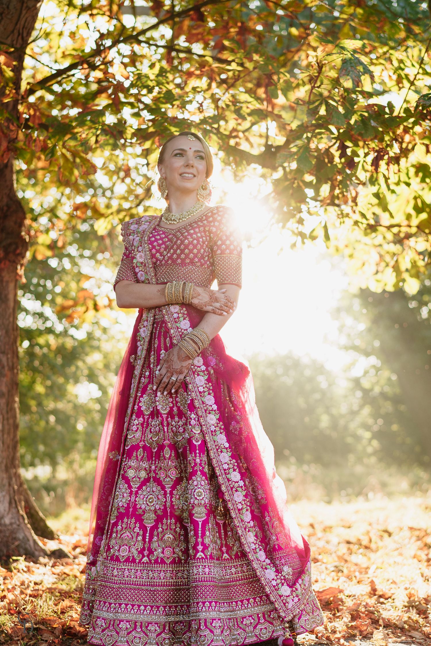 Stunning pink and gold embroidered lehenga captured in golden sunlight under autumn trees.