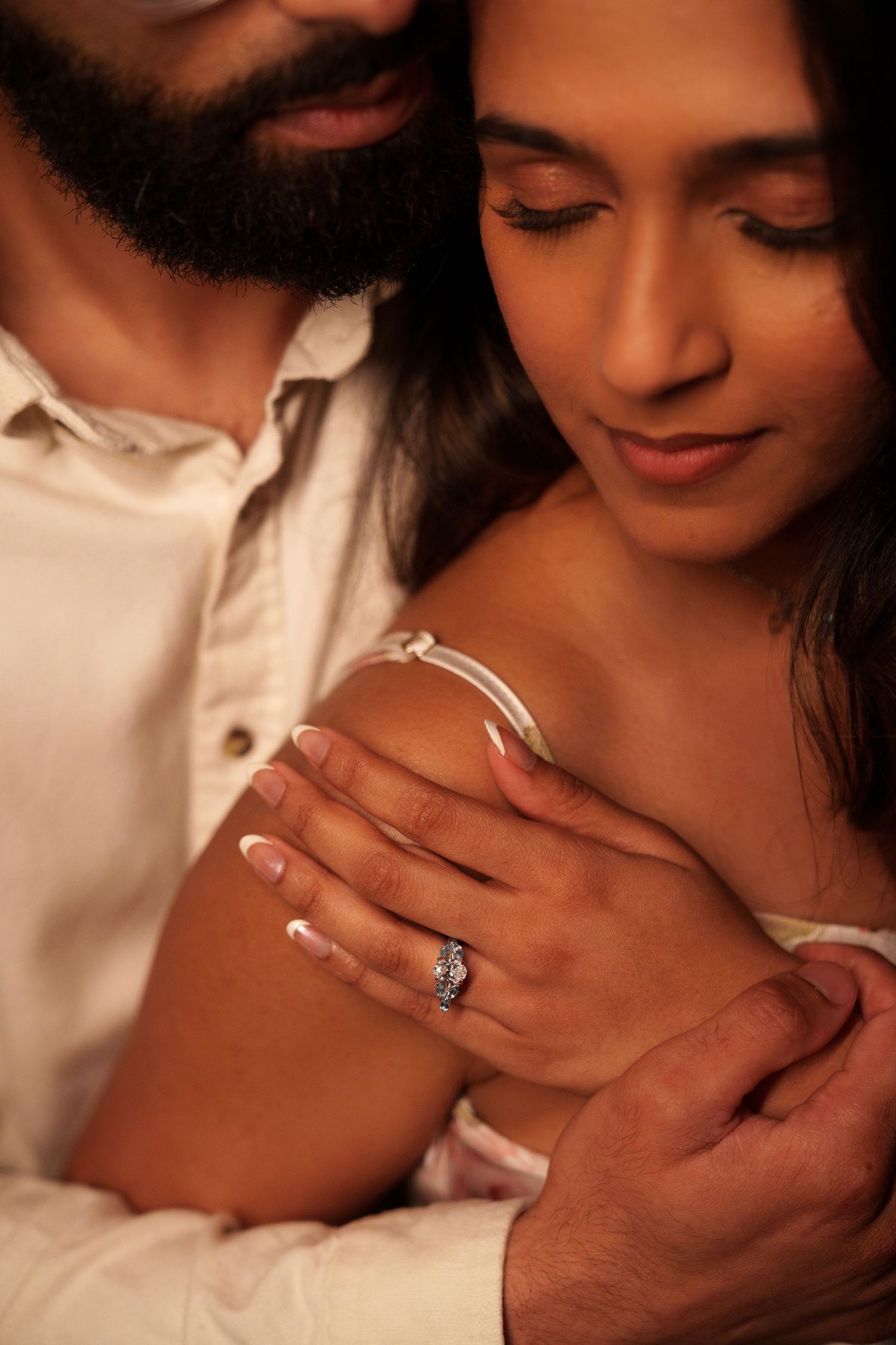 A romantic close-up shows hands embracing with a sparkling engagement ring visible in warm lighting.