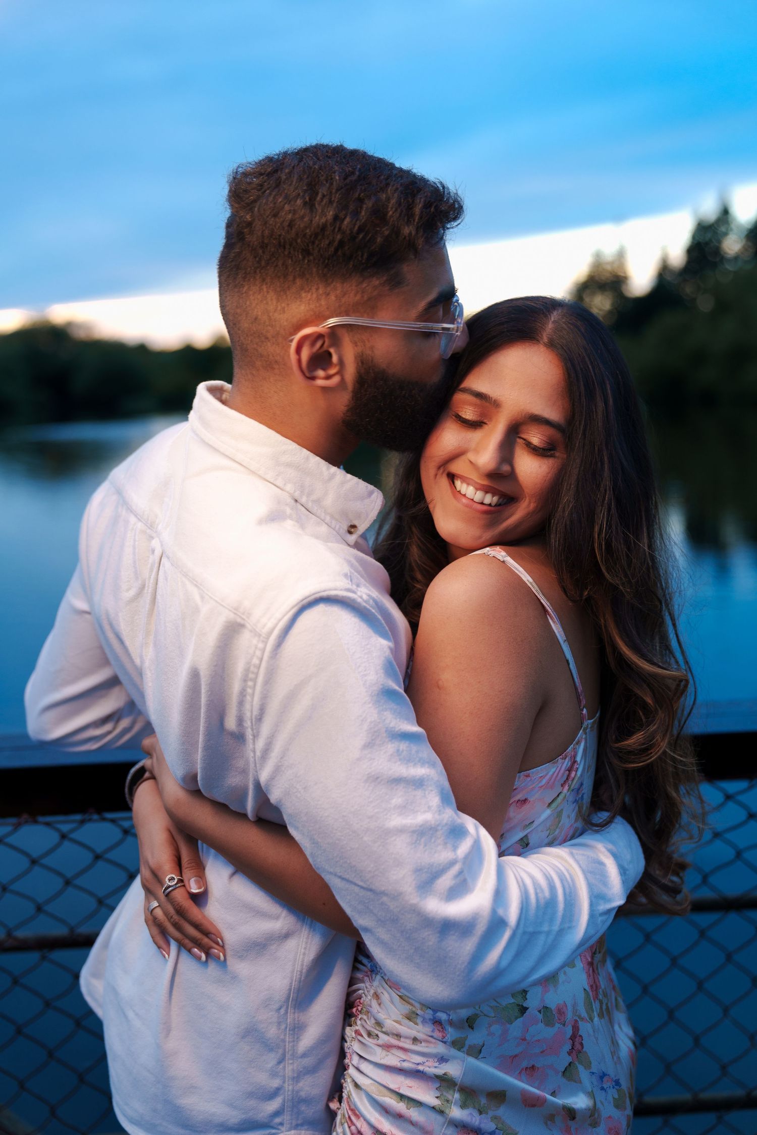 Happy couple sharing intimate moment on lakeside bridge during blue hour.