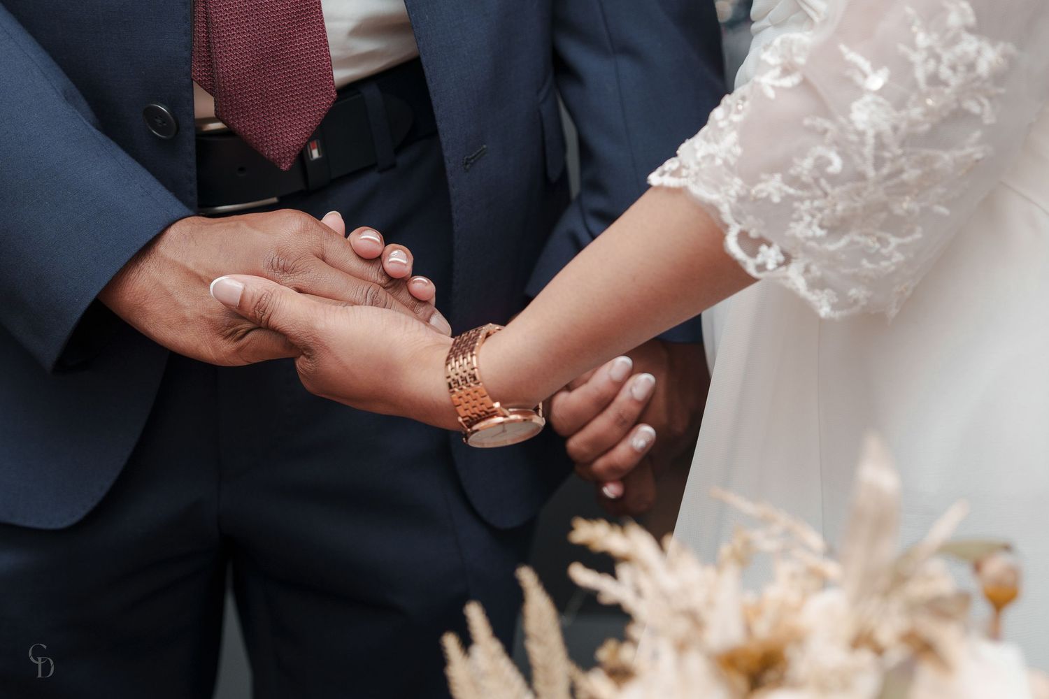 Close-up of hands exchanging wedding rings during ceremony with dried pampas grass decor in background.