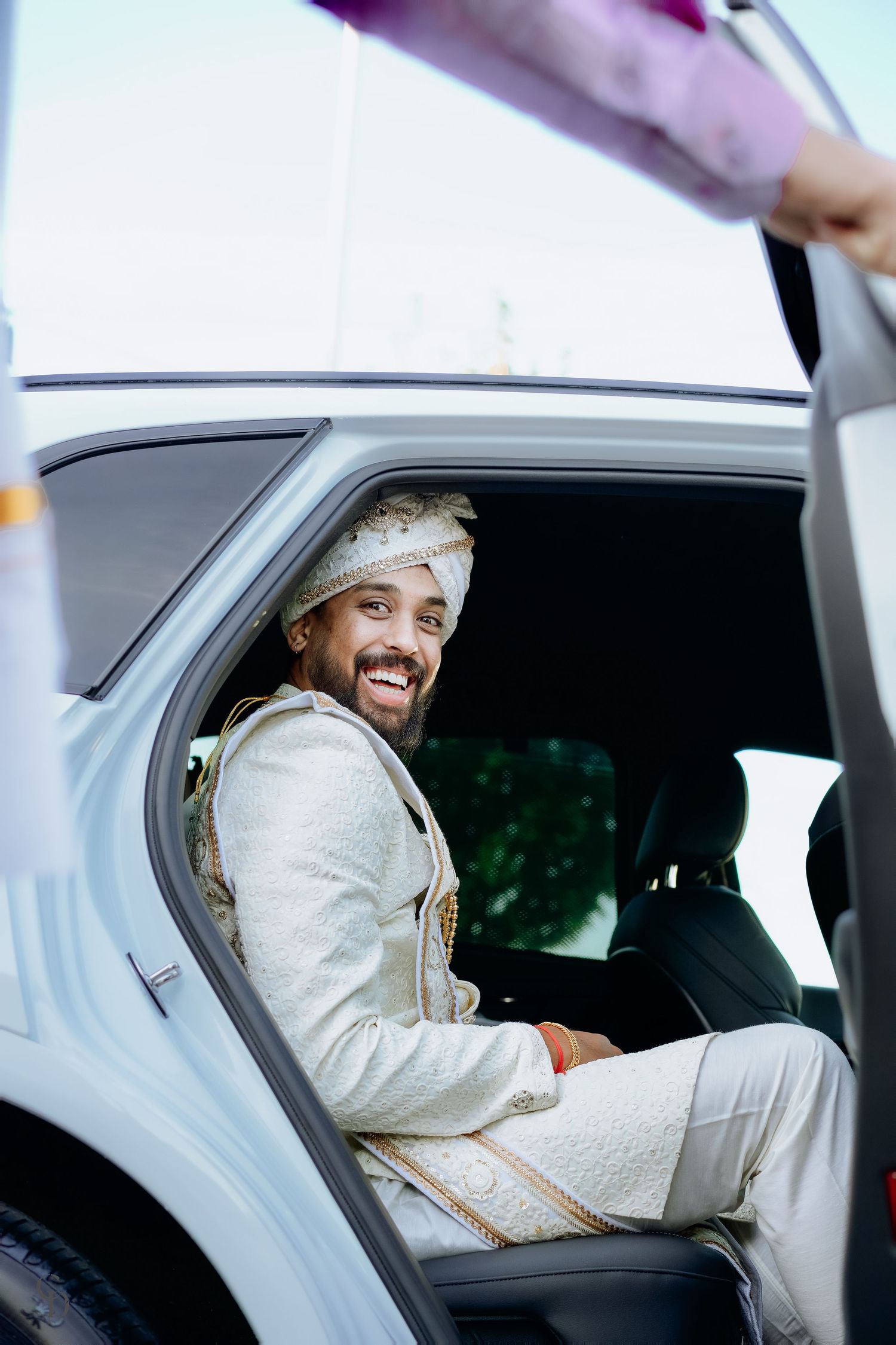 Person in traditional white Indian wedding attire sitting in a car.