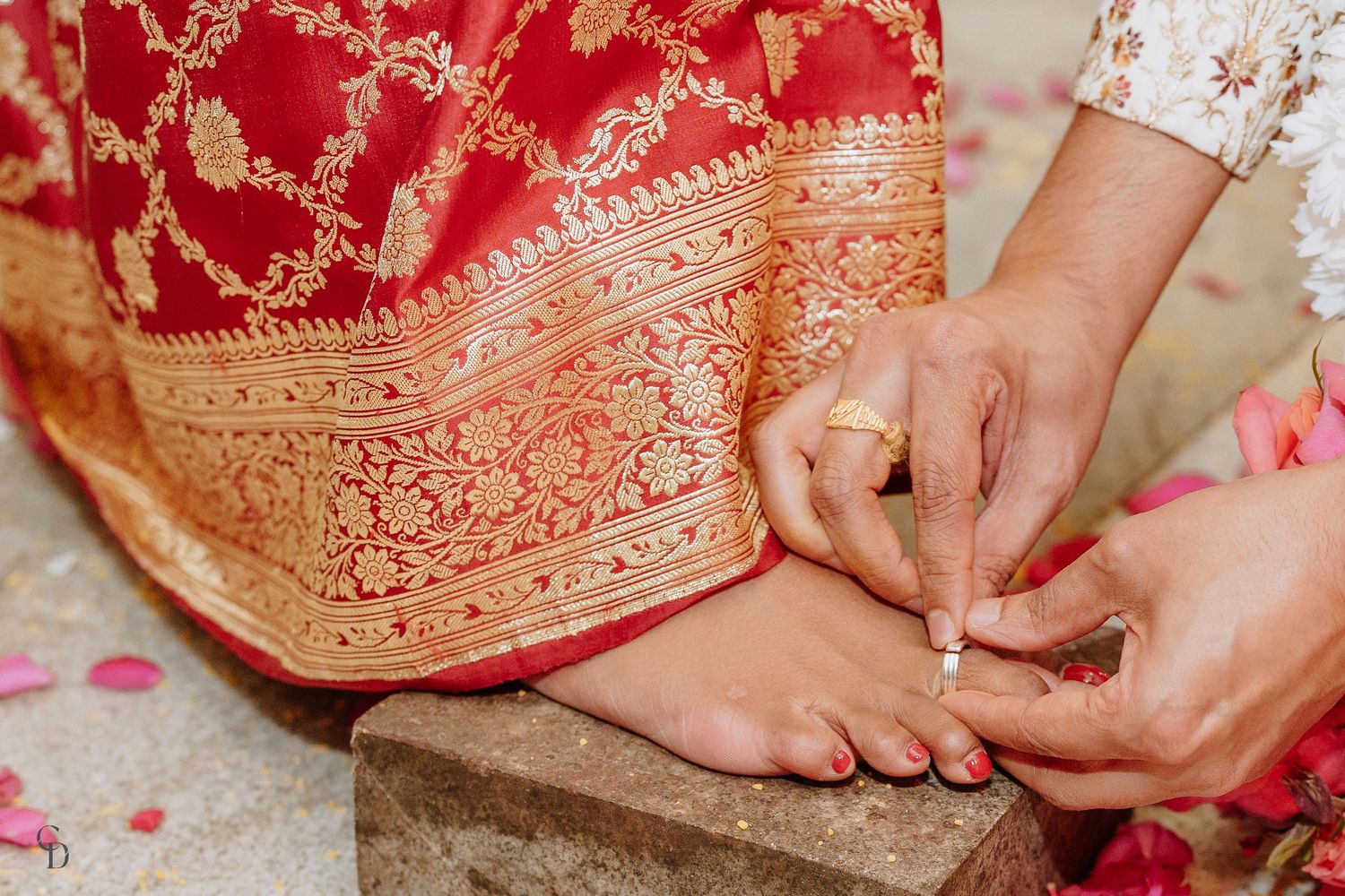 Close-up of traditional toe ring ceremony with golden embroidered sari fabric.