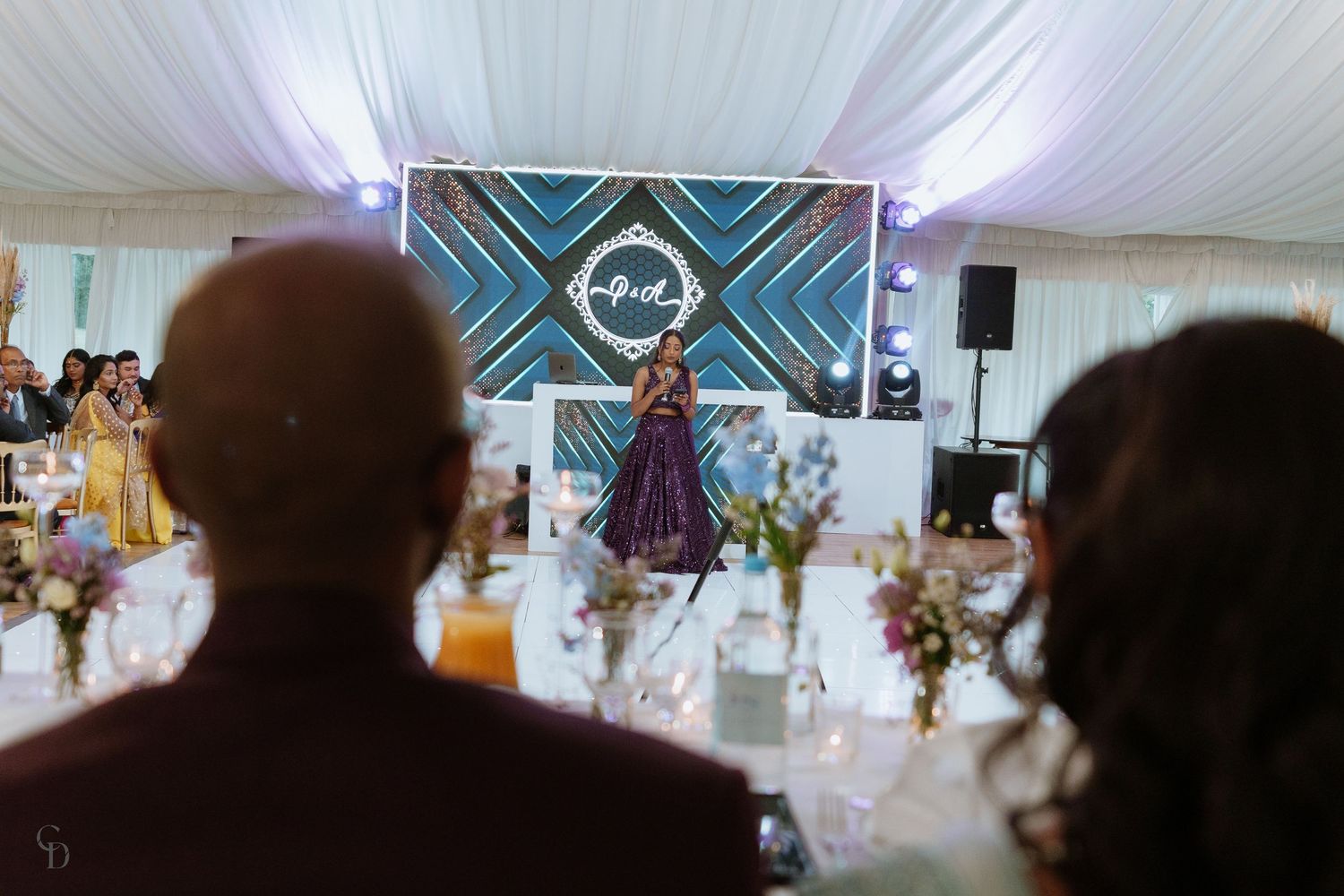 Wedding reception venue with geometric backdrop and purple lighting seen from guests' perspective.