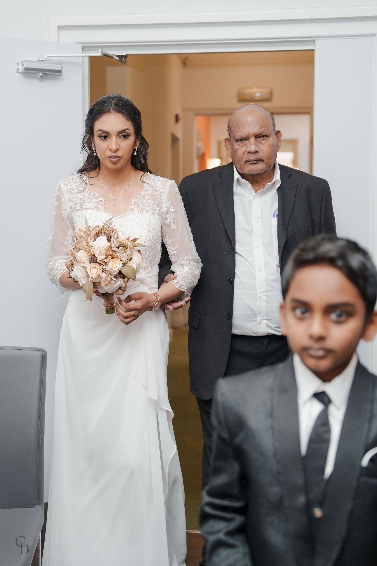 A bride in white gown holding a bouquet stands with family members before the ceremony.