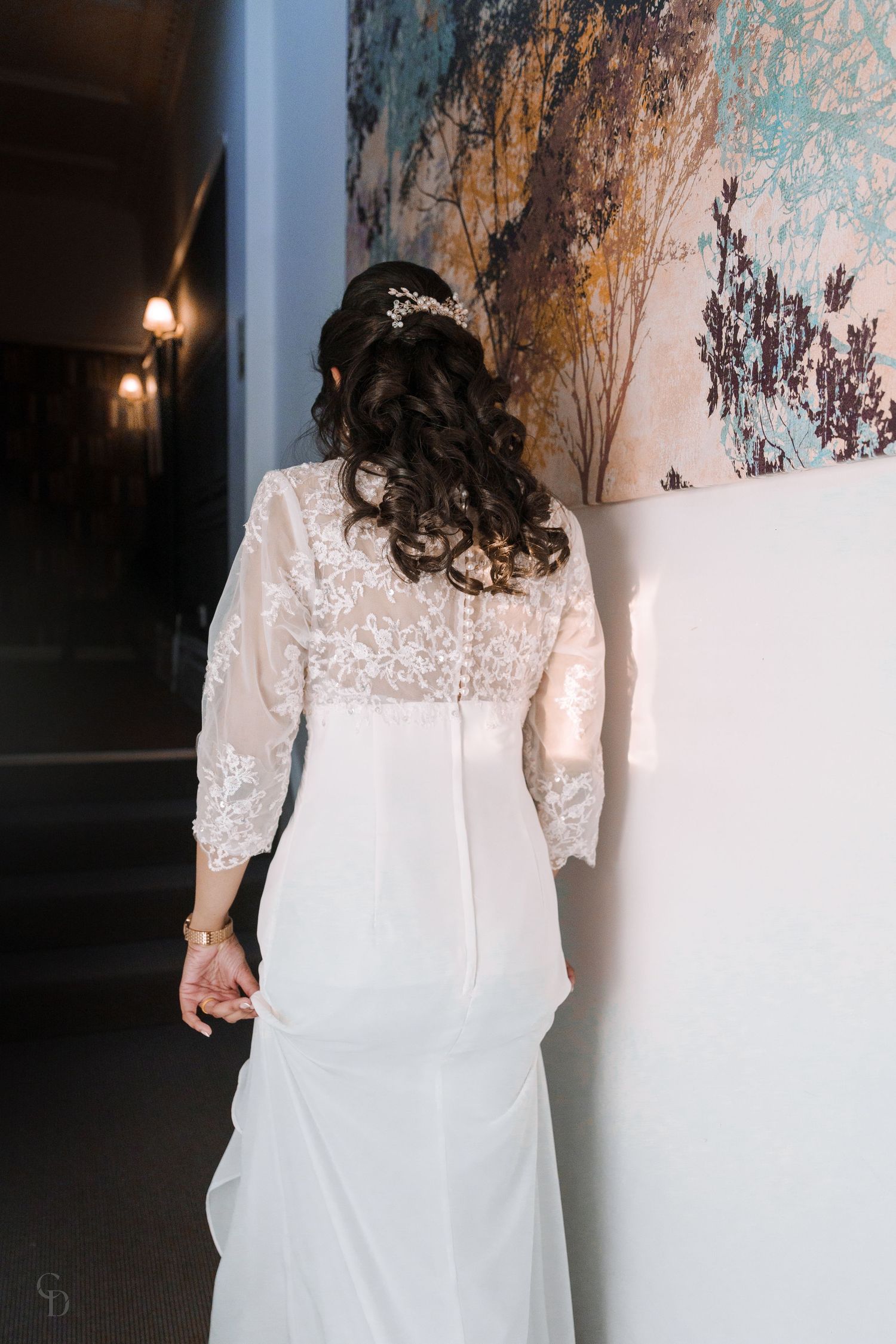 Back view of a wedding dress showing intricate lace details and flowing white fabric.
