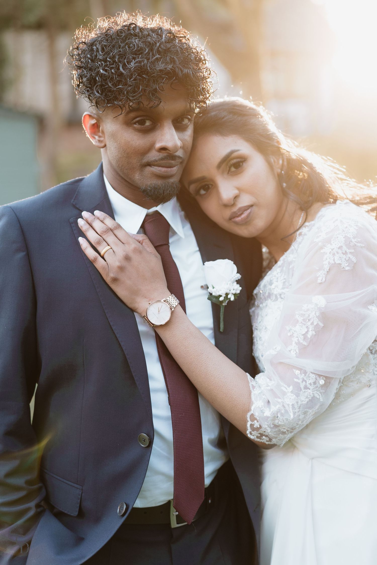 A romantic sunset wedding portrait showing traditional attire with a bride in white lace and groom in dark suit.