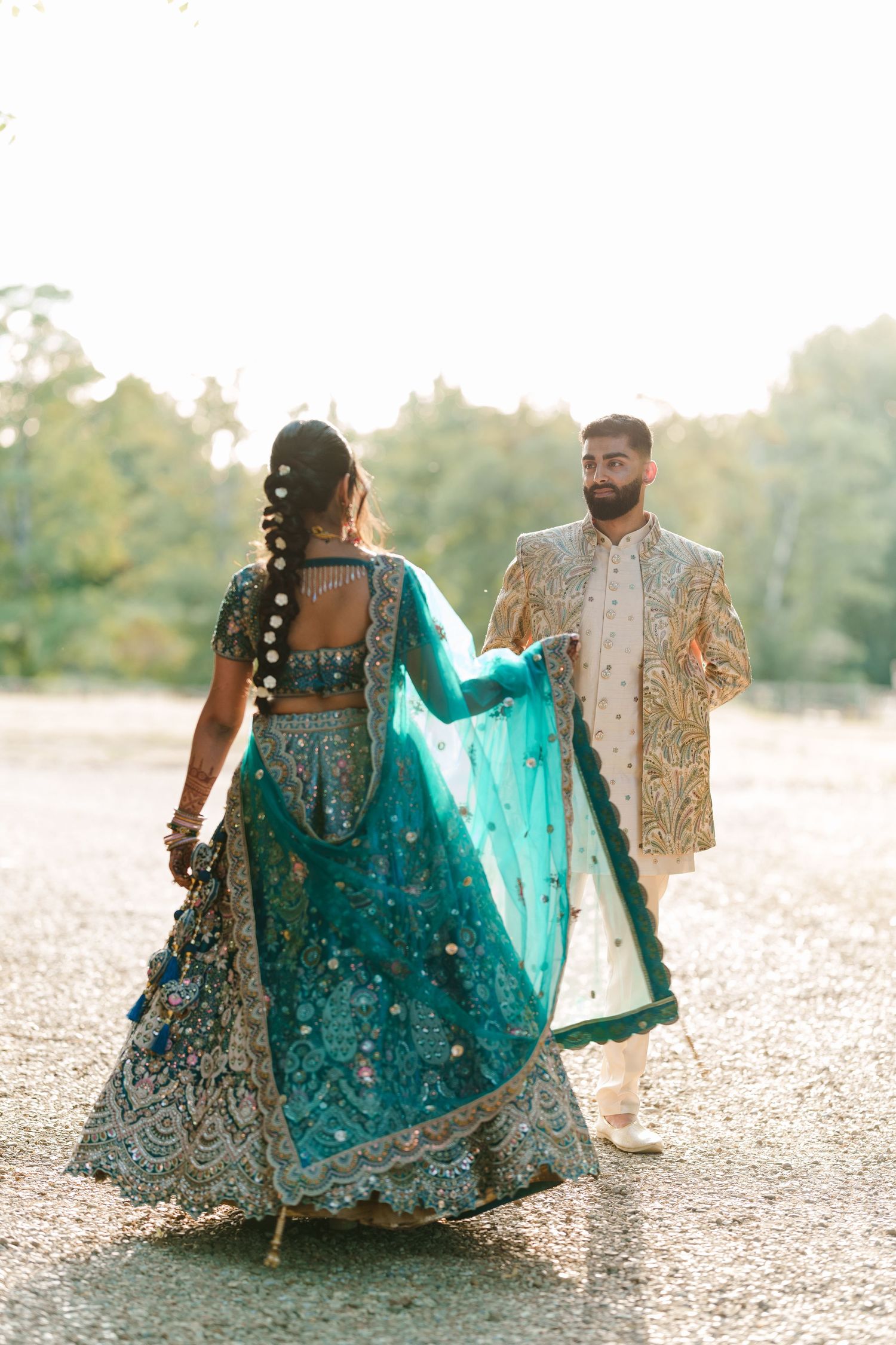A couple in traditional South Asian wedding attire sits on the ground in a romantic outdoor photoshoot sequence.
