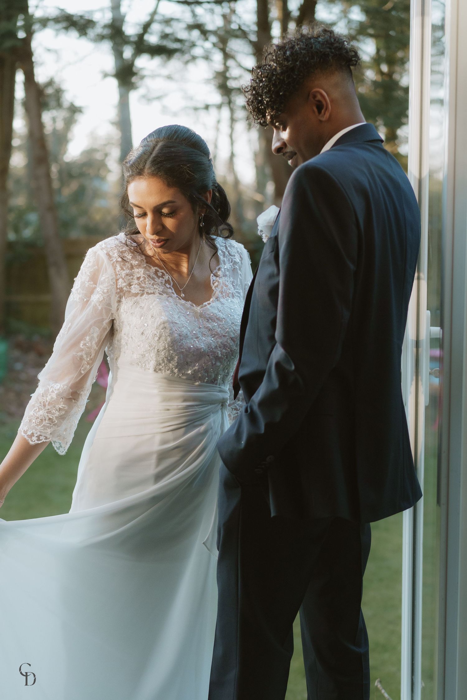 Side view of newlyweds in elegant wedding attire standing together outdoors.