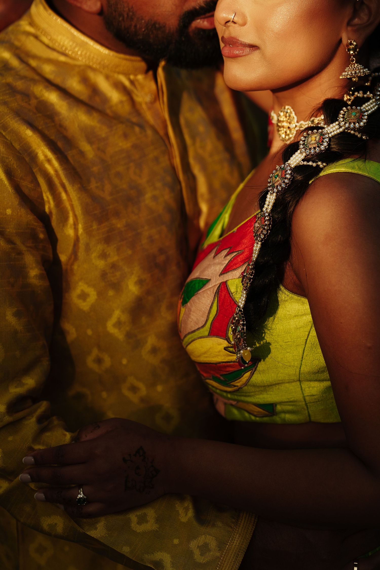 Close-up portrait showing ornate Indian bridal jewelry and green sari detail against textured gold background.