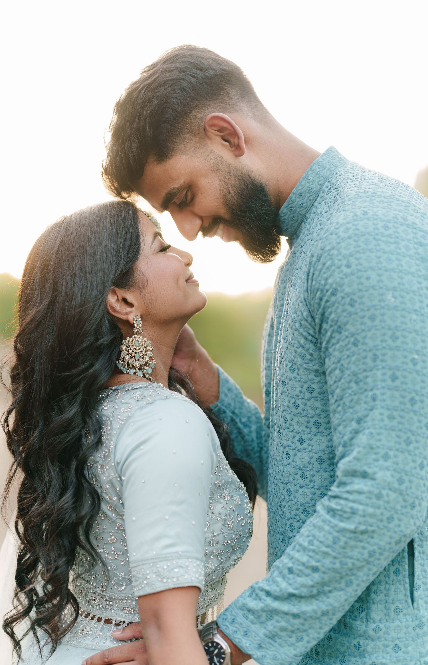 Intimate moment between couple in traditional Indian attire during golden hour outdoors.