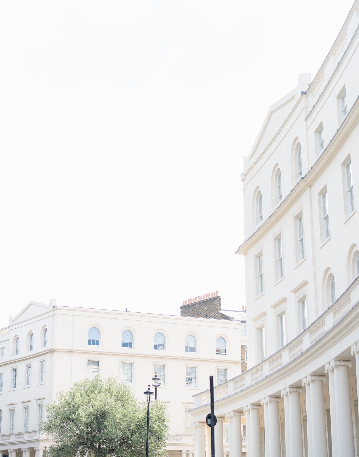 White neoclassical building with curved colonnade and street lamps in soft daylight.