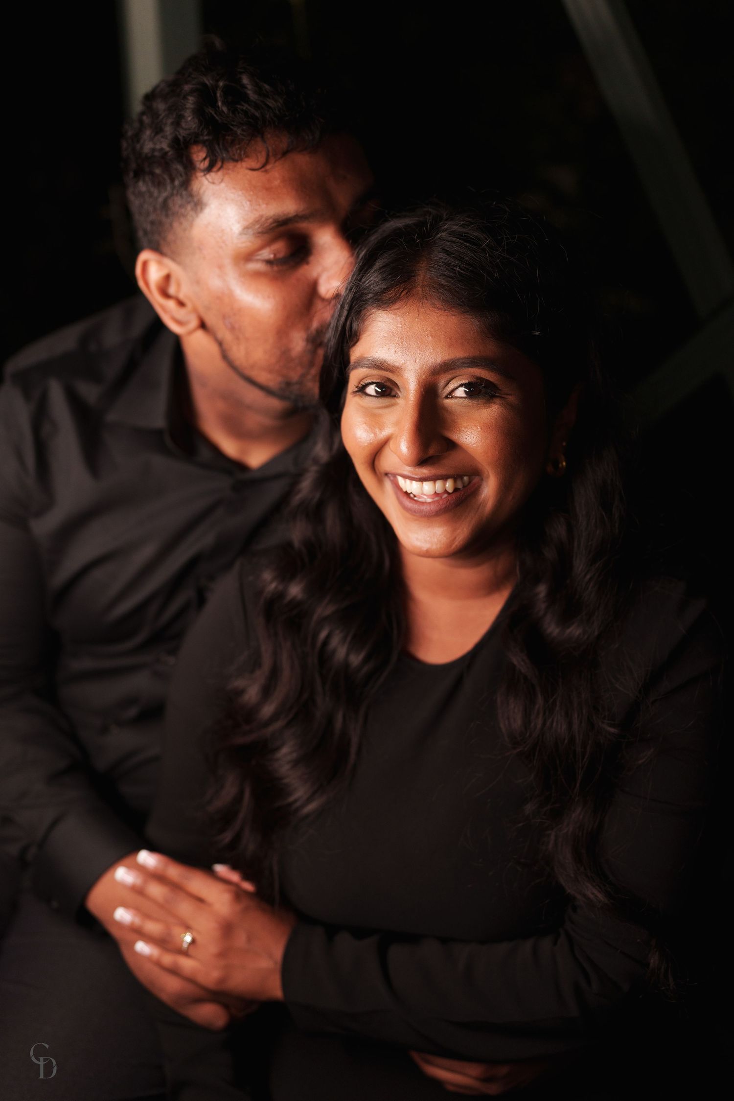 A warm and intimate portrait of a couple in matching black outfits sharing a joyful moment.