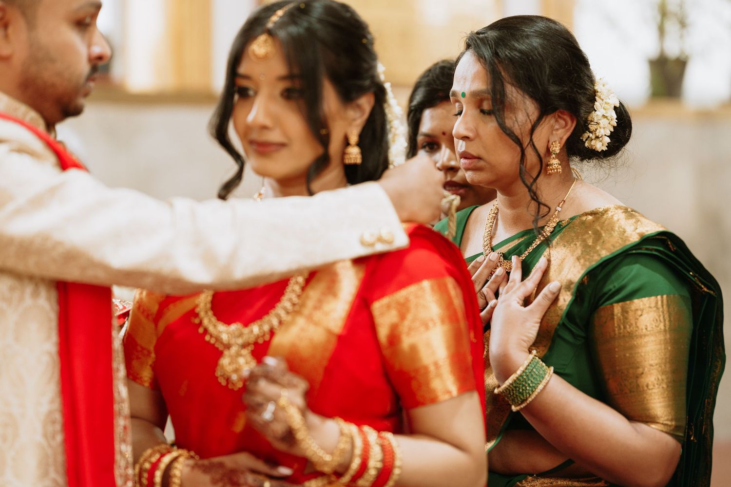 Beautiful bride in traditional Indian attire getting final touches of makeup done while preparing for wedding ceremony.
