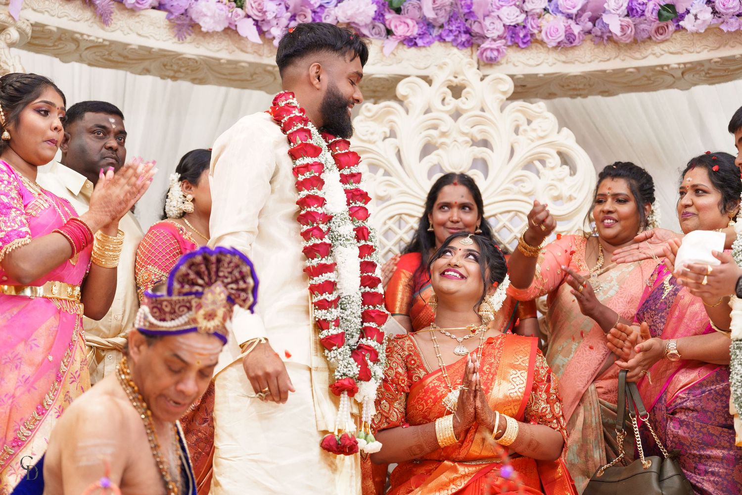 Joyous celebration during Indian wedding ceremony with attendees in vibrant silk saris under floral decorations.