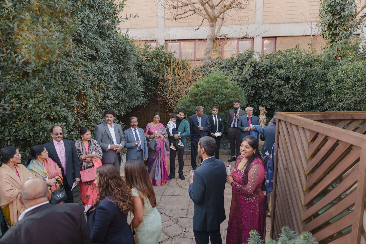 Wedding celebration in outdoor garden setting with guests gathered around couple.