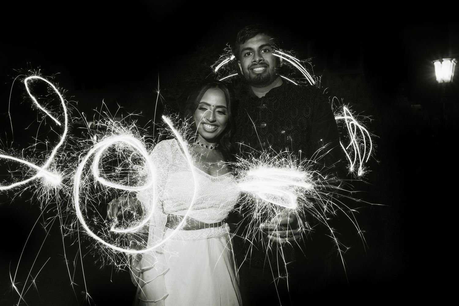 Black and white wedding photo of couple writing LOVE with sparklers at night.