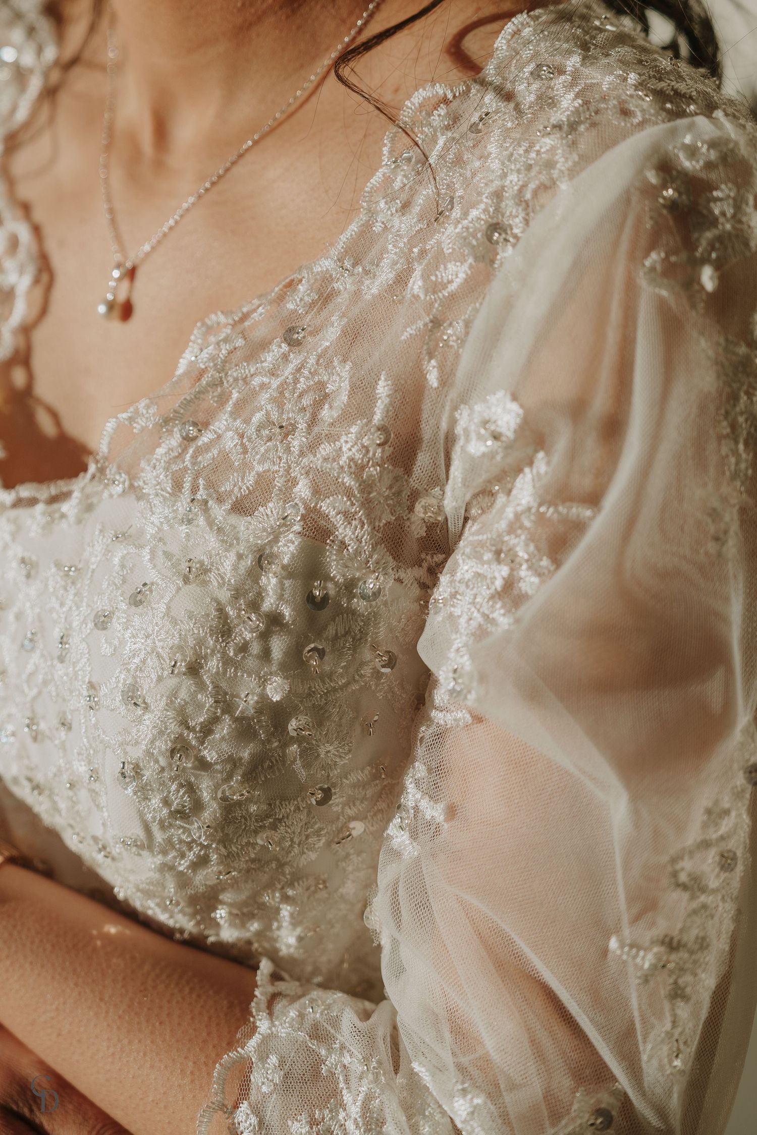 Close-up detail of delicate lace and beadwork on a white wedding dress bodice.