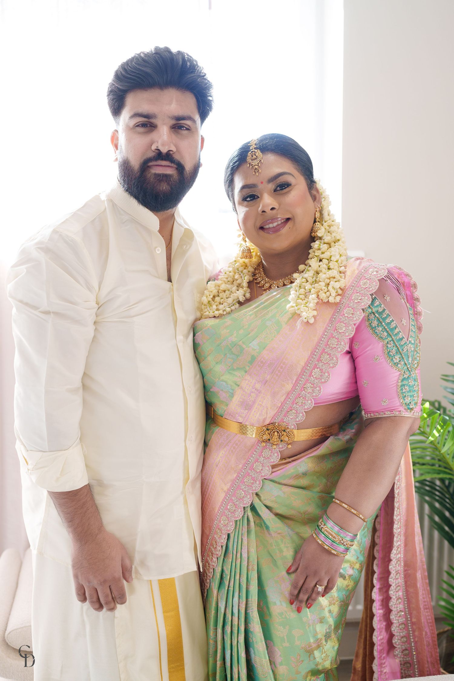 Couple in traditional South Asian wedding attire with silk saree and jasmine flower garland.