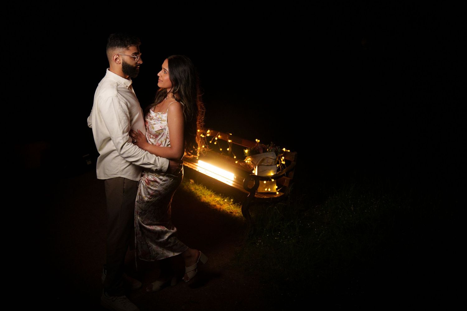 Romantic couple embraces in darkness with glowing light trails creating magical nighttime atmosphere.