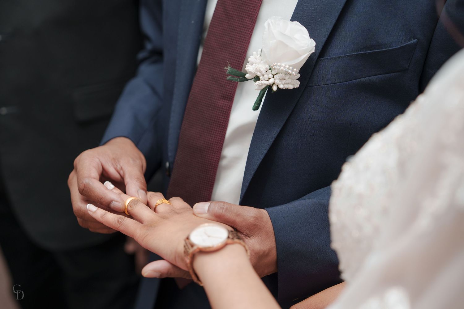 Close-up shot of exchanging wedding rings with white lace sleeve and navy suit details.