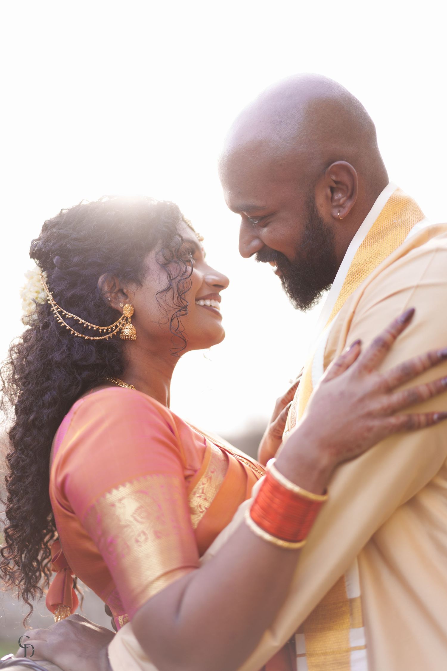 A joyful wedding portrait of a couple in traditional South Asian attire during golden hour.