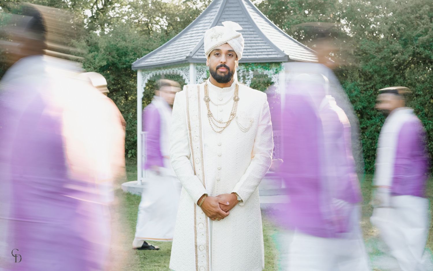 Person in white traditional attire standing with motion-blurred figures in purple.