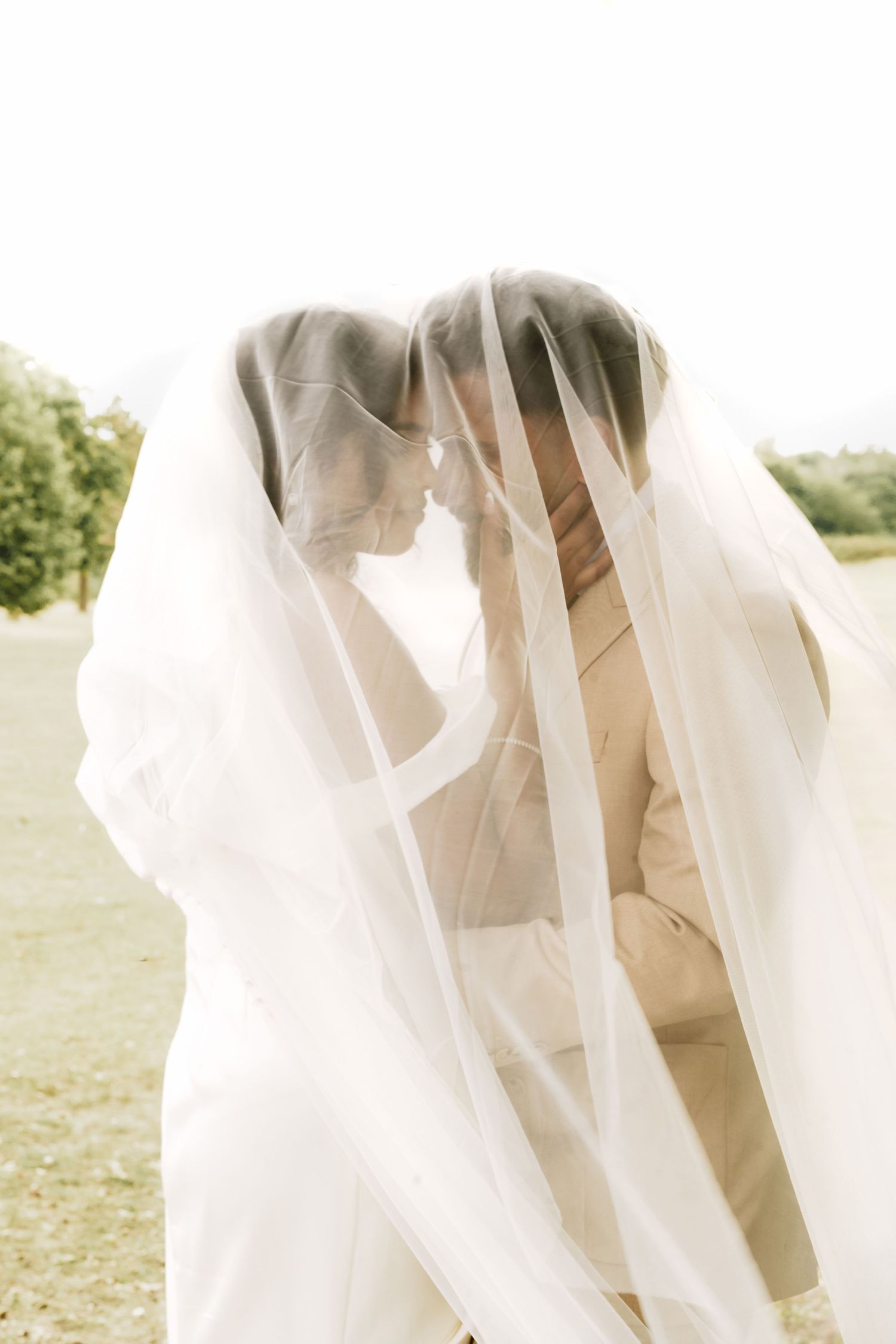 Bride and groom sharing an intimate moment under a flowing white wedding veil outdoors.