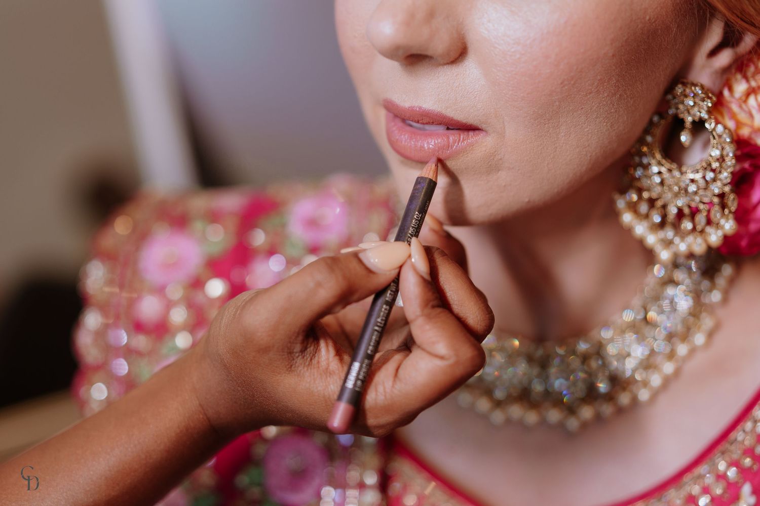 Close-up shot of makeup artist applying lipstick with ornate pearl jewelry visible.