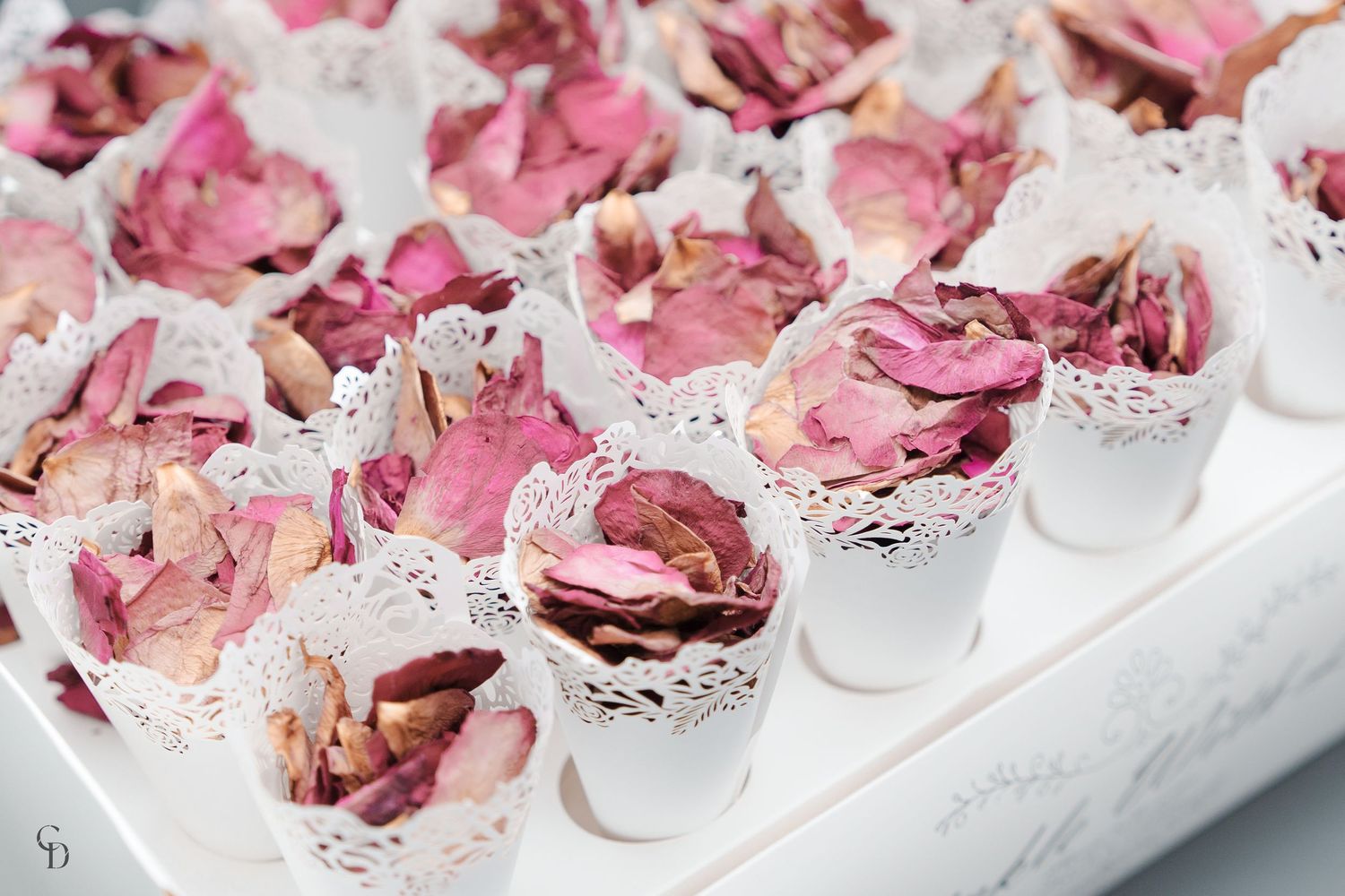 Delicate pink rose petals arranged in small white vessels as elegant wedding decorations.