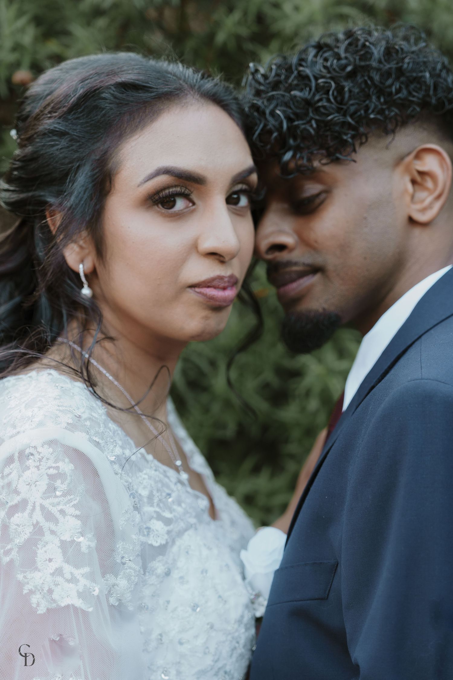 Intimate wedding portrait of couple in white dress and navy suit against nature backdrop.