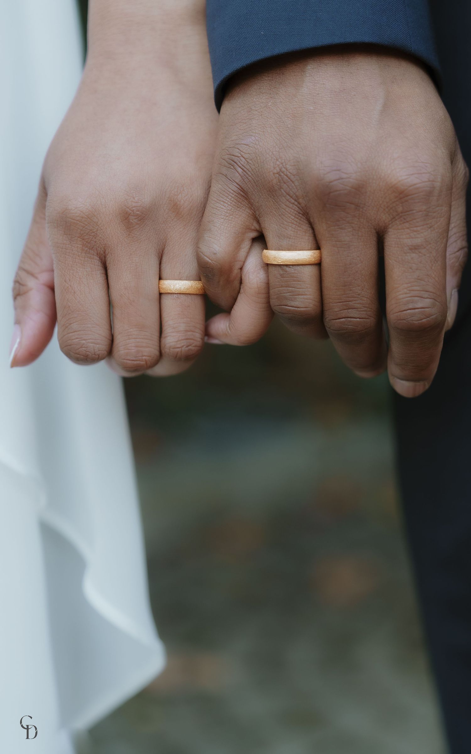 Close-up of bride and groom's hands showing matching wedding bands against white dress.