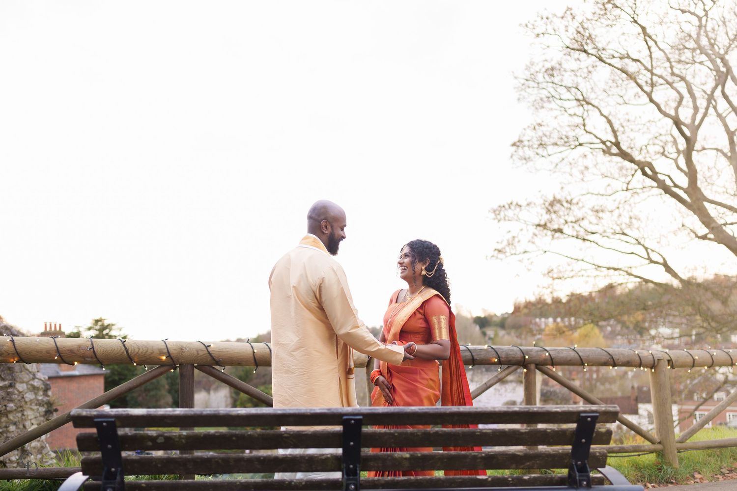 A couple sitting on a park bench wearing traditional Indian formal attire against a nature backdrop.