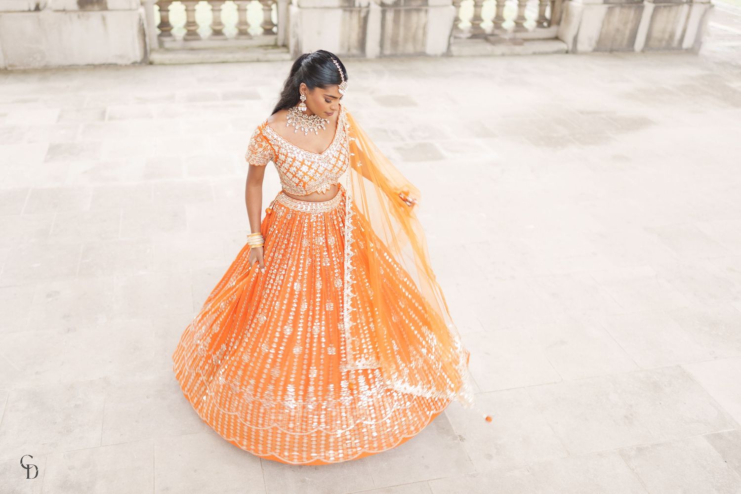 Orange and white sequined lehenga dress photographed from above on a light marble floor.