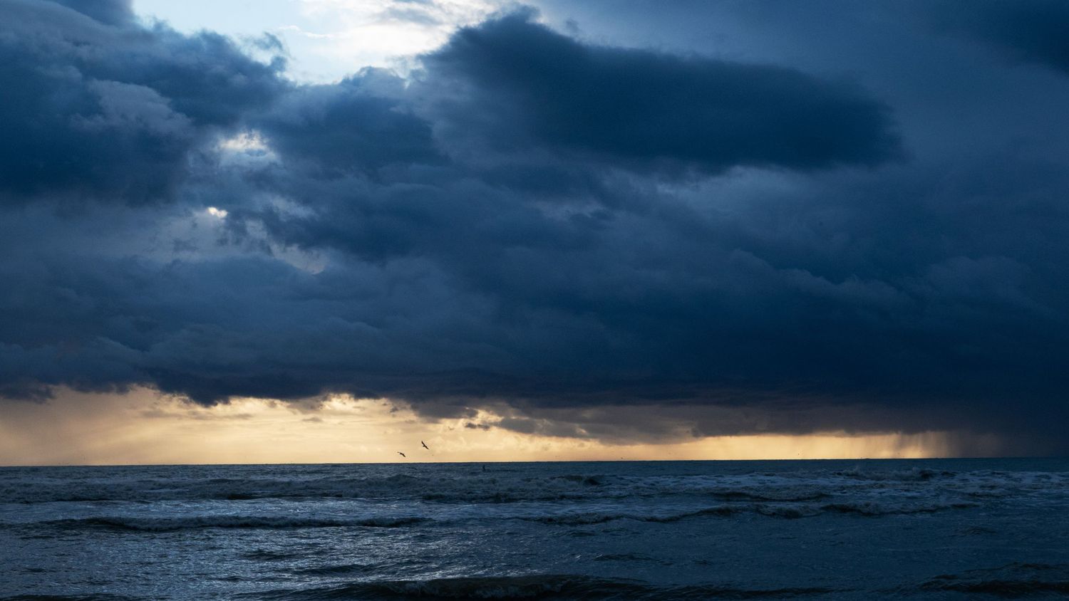 Dramatic stormy seascape with dark blue clouds over calm ocean waters at dusk.