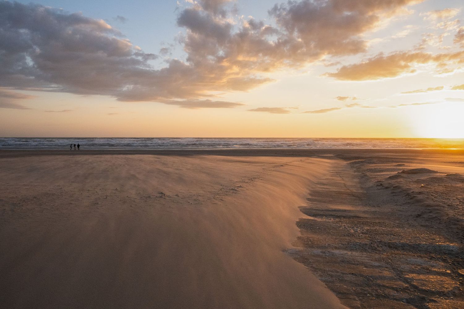 Stunning sunset over a vast sandy beach with gentle waves and two distant figures walking along the shoreline.