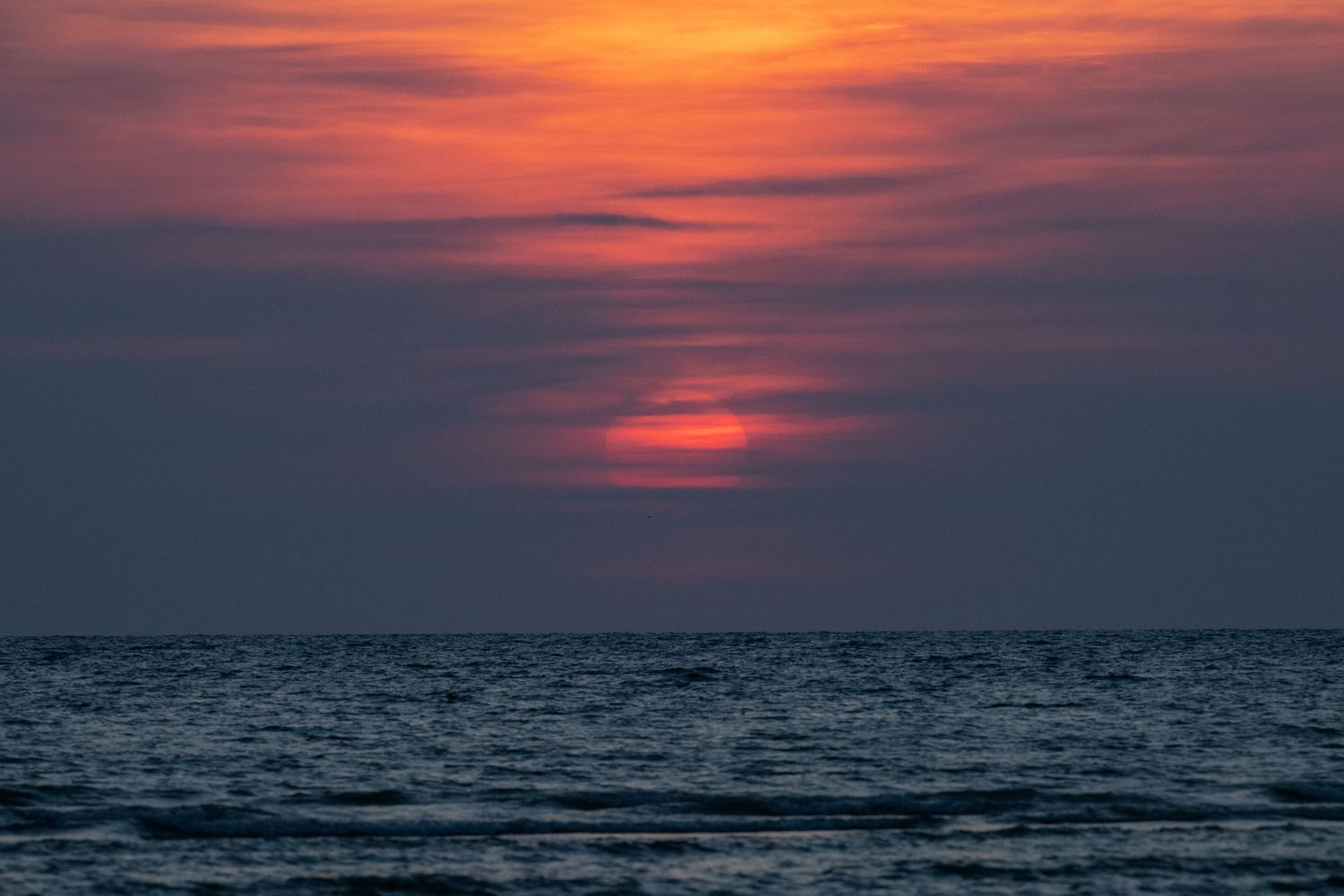 Stunning ocean sunset with vibrant red and orange sky reflecting over calm dark blue sea waters.