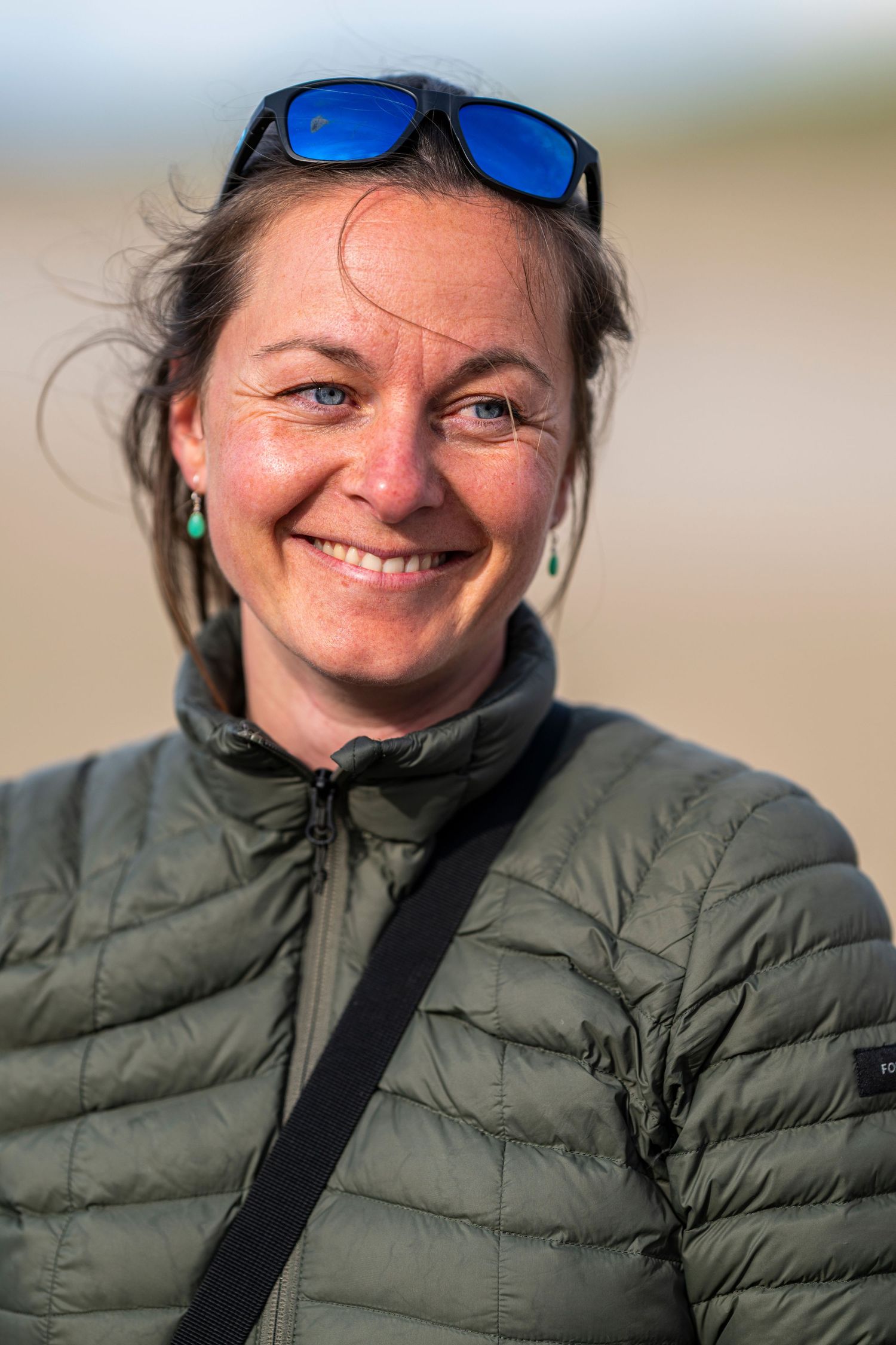 A person wearing a green puffy jacket and blue sunglasses smiles warmly at the camera in a series of candid shots.