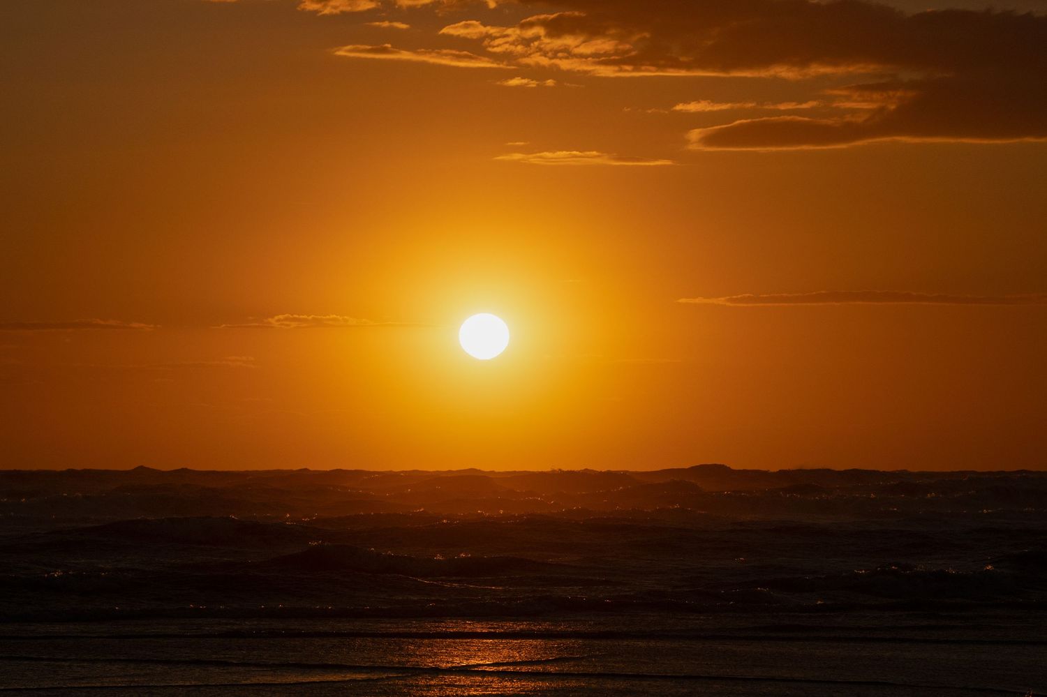 Golden sunset over ocean waves with vibrant orange sky and glowing sun on the horizon.