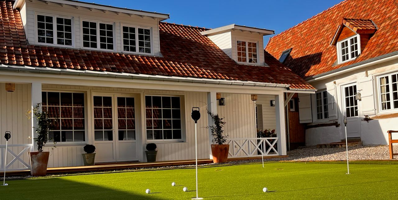 Panoramic view of a white colonial-style building with multiple windows and a vibrant red-tiled roof.
