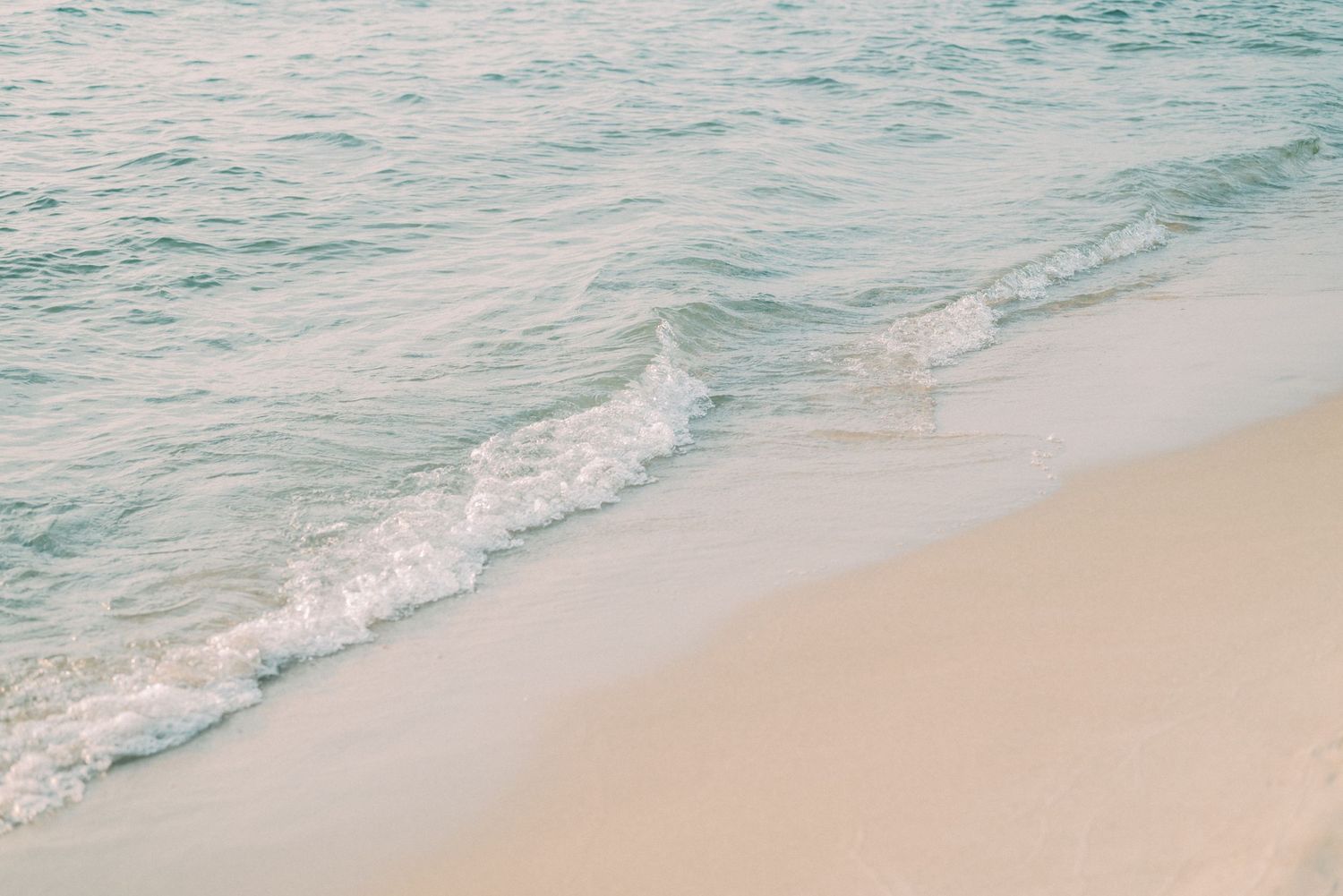 Gentle turquoise waves wash onto pristine beige sand at the shoreline of a serene beach.